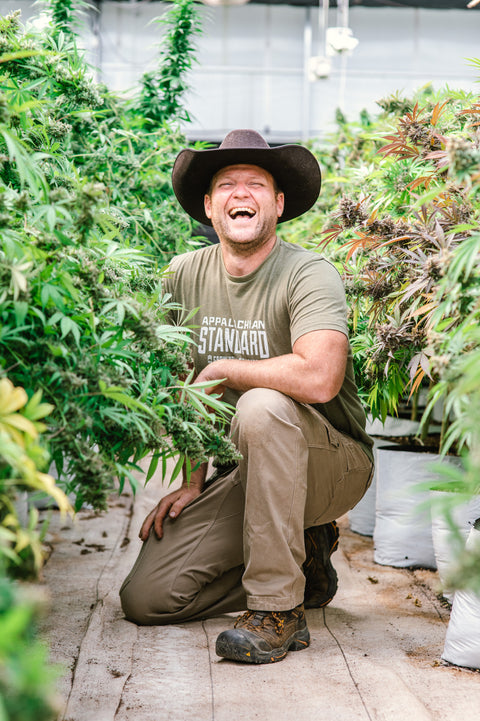 Jesse Ross, owner of Appalachian Standard, laughs while kneeling down surrounded by hemp plants