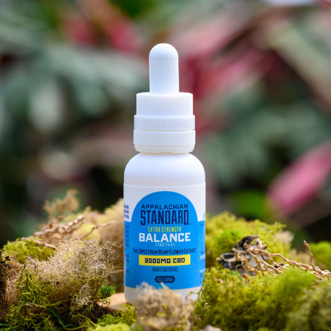 A 1 oz bottle of Appalachian Standard's Balance Extra Strength CBD Tincture on a small wooden platter surrounded by moss