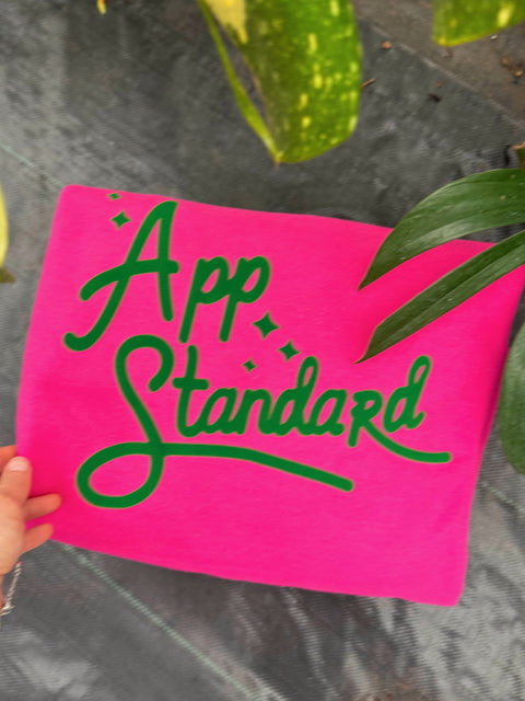 Appalachian Standard pink and green sweatshirt in the greenhouse around green plants.