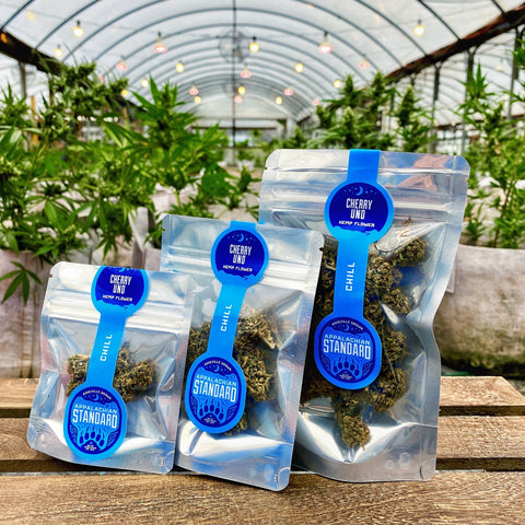 Cherry Uno Hemp Flower in three different sized packages sitting on a wood crate in the Appalachian Standard greenhouse.