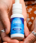 Two white hands hold a 1 oz bottle of Appalachian Standard's Chill CBD + CBN Tincture
