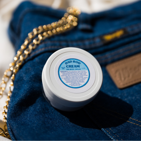 Appalachian Standard Dad Bod Cream, 1.5 oz jar, with 188mg CBD, styled on a pair of Wrangler jeans, next to a gold chain.