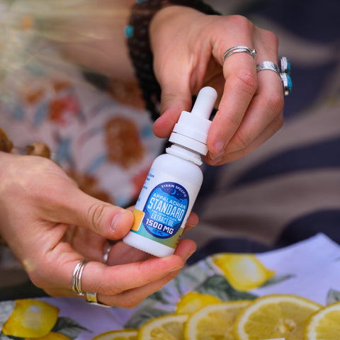 Fiddyshadesofgreen holding a bottle of Lemon Cheesecake hemp tincture over slices of lemons.