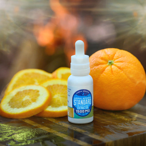 A bottle of Appalachian Standard's Orange Chai Hemp Oil Tincture on a wooden table with an orange and orange slices behind it.