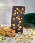 A bar of Appalachian Standard's Caramel Bliss Cookie CBD Chocolate with cookies in the front and a green hat in the back