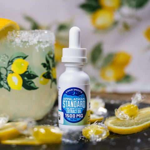 A 30 ml bottle of Appalachian Standard's Lemon Drop CBD Tincture on a table surrounded by lemons and lemon drop candy