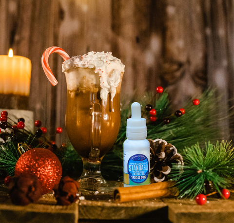 A glass of hot chocolate with whipped cream and a candy cane next to a 1 oz bottle of Appalachian Standard's Peppermint Mocha CBD Tincture