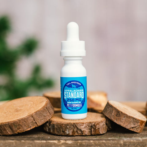 A 15 ml bottle of Appalachian Standard's Pet Formula Full Spectrum 250 MG CBD Tincture sits on a piece of wood