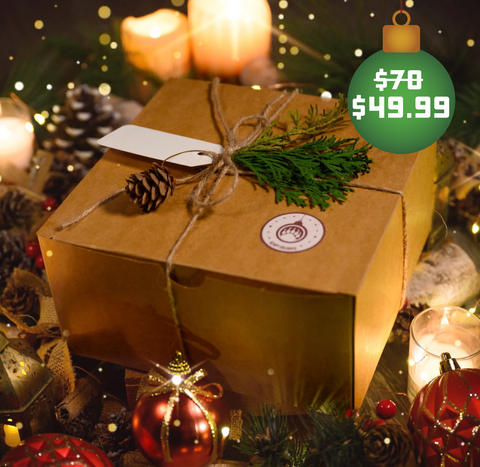 A brown box wrapped with twine, pine leaves, and a pine cone surrounded by Christmas decorations
