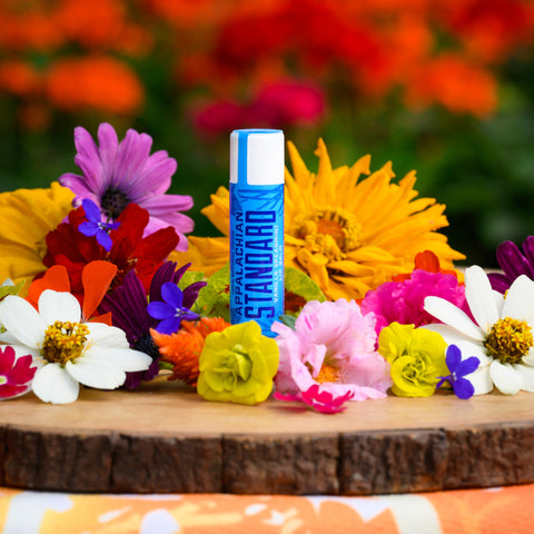 A stick of Appalachian Standard's Vanilla Spearmint CBD Lip Balm on a piece of wood surrounded by flowers