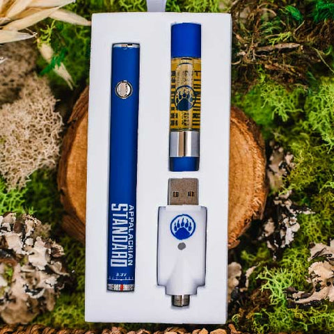 Appalachian Standard's Cherry Uno CBD Vape kit in box on a wood slice surrounded by green moss
