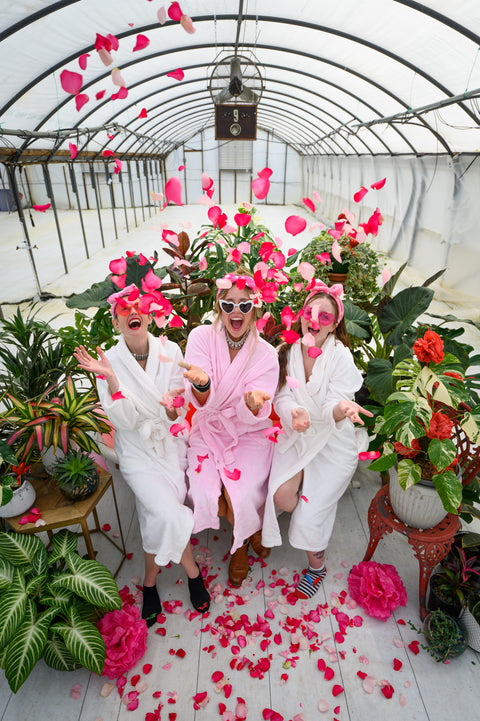 Maegen, Lauren, and Heather throw petals in the air in the greenhouse