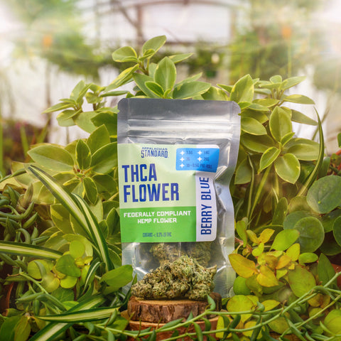 THCA Berry Blue Flower is a mylar bag with a label on a background of green plants with hemp flower in front.