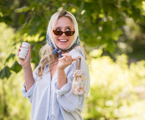 Woman in a light outfit with a scarf and sunglasses, standing outdoors holding CBD Appalachian Standard Body Cream bundle.
