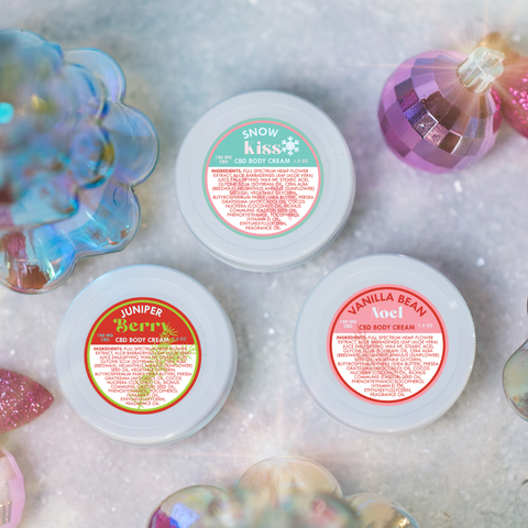 Three jars of body cream with colorful labels on a textured surface with decorative elements.