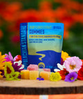 A bag of Appalachian Standard's All-Natural CBD Gummies and pieces of the CBD gummies on a wooden platter surrounded by flowers