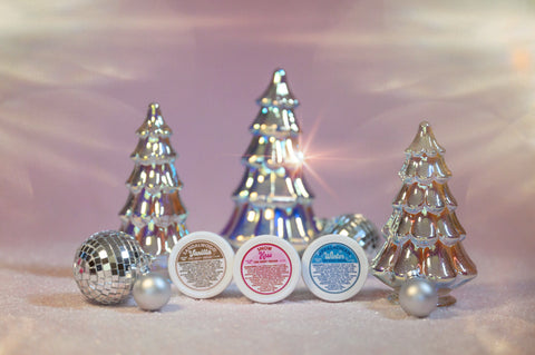 A photo of Appalachian Standards Holly Jolly Hydration Set, featuring their Limited Edition body creams, sandalwood vanilla, snow kiss, and Appalachian winter. The photo has the body creams surrounded by shiny glass tree decorations, disco balls and ornaments.