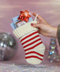 A photo of Appalachian Standards Kris Kringles' CBD Chocolate Stocking. This bundle includes their Limited Edition Teeny Weeny Marshmallow CBD Chocolate, Raspberry Almond, Salted Croissant, and Caramel Macchiato. The Chocolate bars are placed in a white and red striped stocking with shiny glass christmas tree decorations, disco balls, and ornaments in the background.