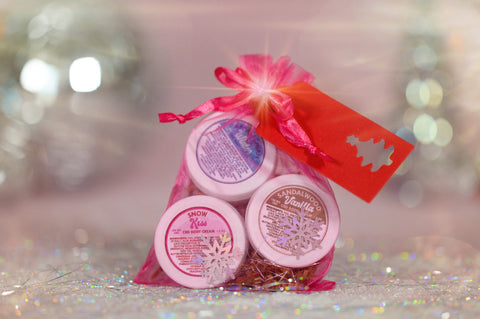 A photo of Appalachian Standards Holly Jolly Hydration Set, featuring their Limited Edition body creams, sandalwood vanilla, snow kiss, and Appalachian winter. The body creams are bundles in  pink mesh bag with a red Christmas tag.