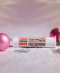 A photo is Appalachian Standards Peppermint Mocha CBD Vape Cartridge surrounded by snow and pink ornaments.