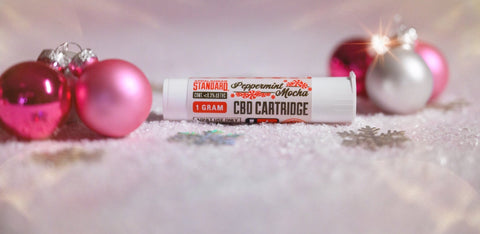 Appalachian Standard's CBD Peppermint Mocha Vape Cartridge in front of Christmas ornaments on top of fake snow.