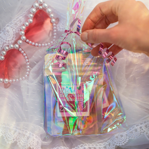A hand reaching for a bag of candy on a white lace fabric with pink heart shaped sunglasses