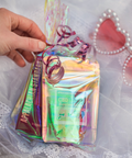 A hand reaching for a clear bag with bags of candy inside on a white lace fabric with pink heart shaped sunglasses