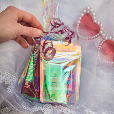 A hand reaching for a clear bag with bags of candy inside on a white lace fabric with pink heart shaped sunglasses