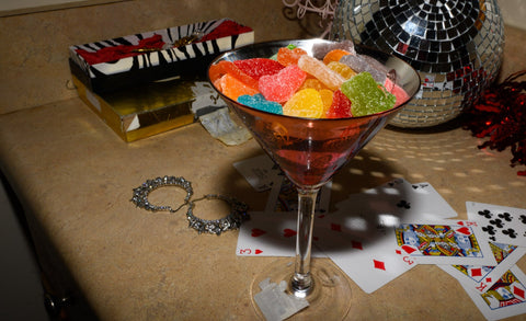 Appalachian Standard CBD Boujee Bear gummies in a pink martini glass on top of a stack of playing cards with a disco ball in the background.