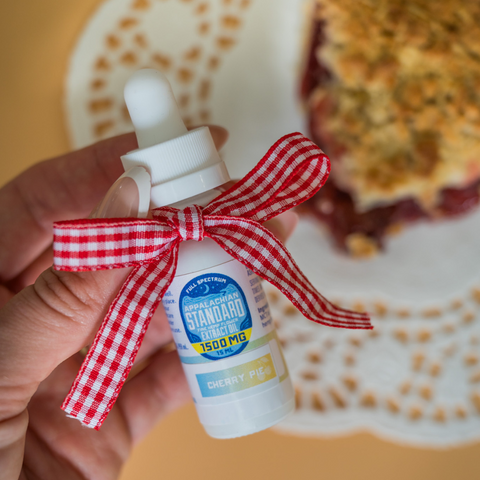 Bottle of supplement with a red and white checkered ribbon held by a hand, with a blurred background.