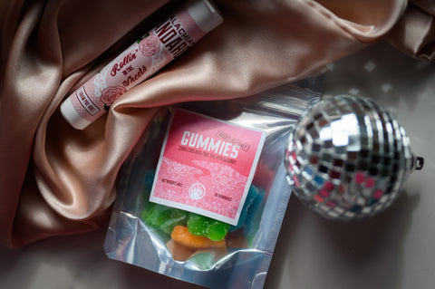 Appalachian Standard's Rollin' in the Sheets 1:1 1 Gram Pre-Roll and Altitude Adjusting gummies in a bag, on a white table with a pink satin sheet and disco ball.