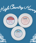 Three Appalachian Standard CBD body cream containers with labels on a blue background, featuring 'High Country Hunny' branding.