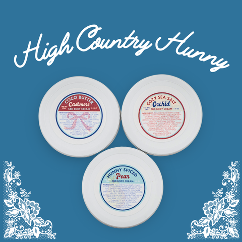 Three Appalachian Standard CBD body cream containers with labels on a blue background, featuring 'High Country Hunny' branding.