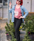Woman with red hair and sunglasses standing among potted plants in an outdoor setting