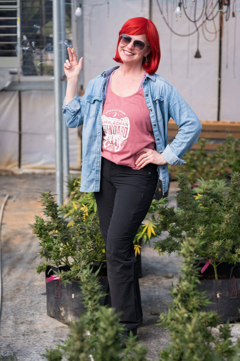 Woman with red hair and sunglasses standing among potted plants in an outdoor setting