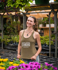 Woman standing among flowers and plants in a greenhouse wearing an 'Appalachian Standard' tank top.