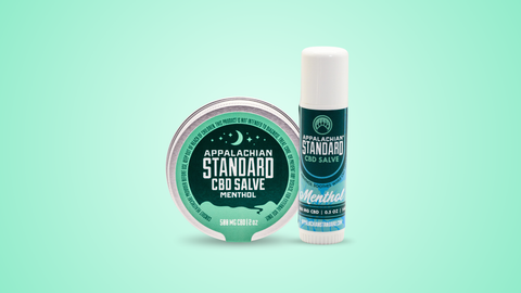 Appalachian Standard's Menthol CBD Salve in a metal tin and white tube with blue/green labels on a blue/green backgroudn