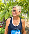 Woman wearing a blue tank top with 'Appalachian Standard' text, standing outdoors with greenery in the background.