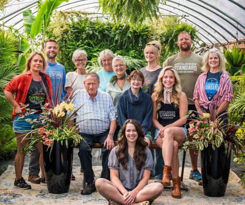 Group of people posing in a greenhouse with plants and greenery.
