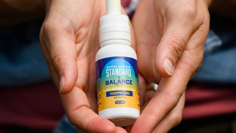 Two white hands cupped together holding a 1 oz bottle of Appalachian Standard's Balance CBD Tincture