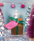 Gift box with a pink tag labeled 'Naughty or Nice' against a festive background with Christmas trees and lights.