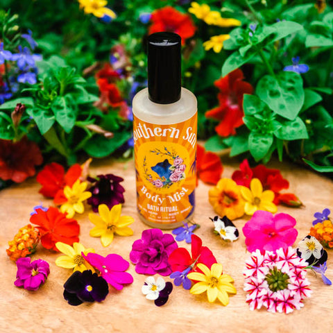 A bottle of Appalachian Standard's Southern Sun Hydrating Body Mist with Aloe surrounded by flowers