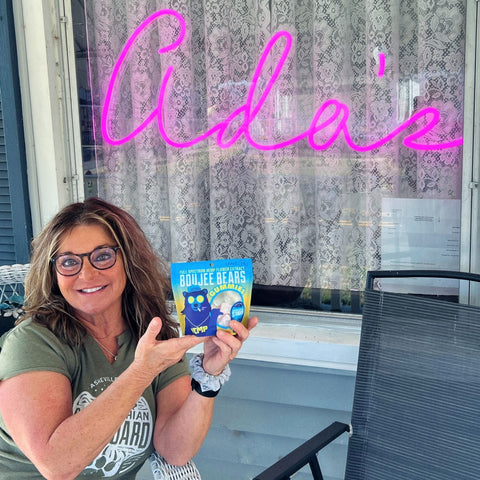 Aunt Sally holding a bag of Boujee Bears CBD Gummies while sitting down on a chair in front of the Ada's sign