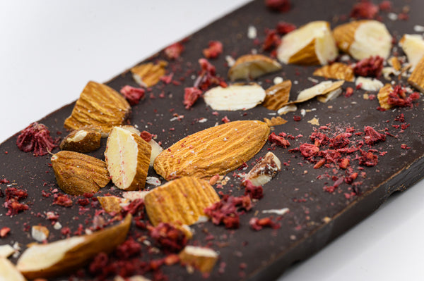 Almonds and raspberries sprinkled on a close-up of a dark chocolate bar on a white background