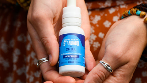 Two white hands hold a 1 oz bottle of Appalachian Standard's Chill CBD + CBN Tincture