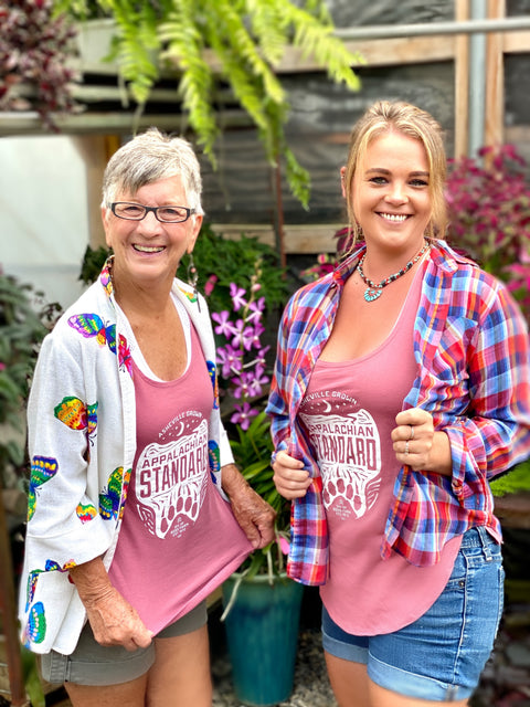 Two women standing in the greenhouse in dusty rose Appalachian Standard tank tops.
