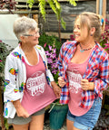 Two women standing in the greenhouse in dusty rose Appalachian Standard tank tops looking at each other