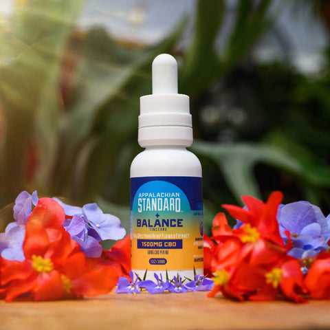 Balance CBD Oil tincture on a wooden counter surrounded by flowers. 