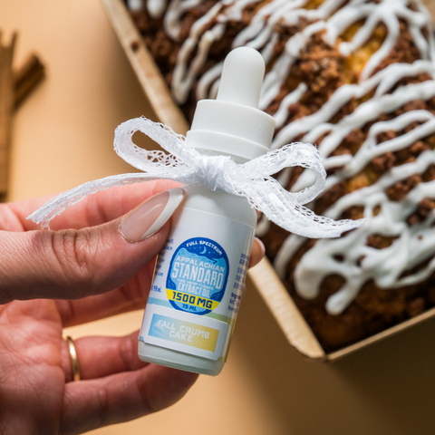 Hand holding a small white bottle with a blue label in front of a cinnamon roll.