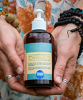 A 4 fl oz bottle of Glow Up Massage Oil with CBD by Appalachian Standard held by Lauren Davis of Fiddy Shades of Green